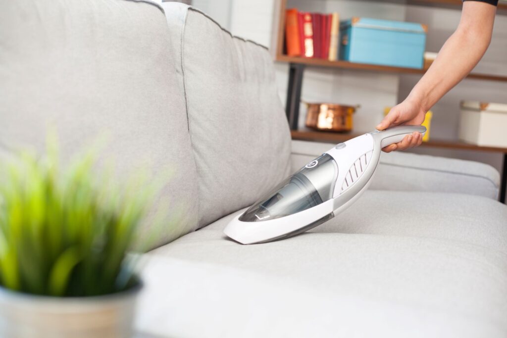Frau mit Handstaubsauger reinigt Sofa