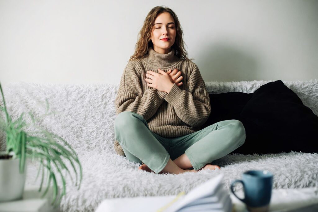 Schöne junge Frau im Lotussitz auf dem Bett beim Üben von Pranayama-Atemtechniken, um nach einem stressigen Tag innere Ausgeglichenheit zu finden