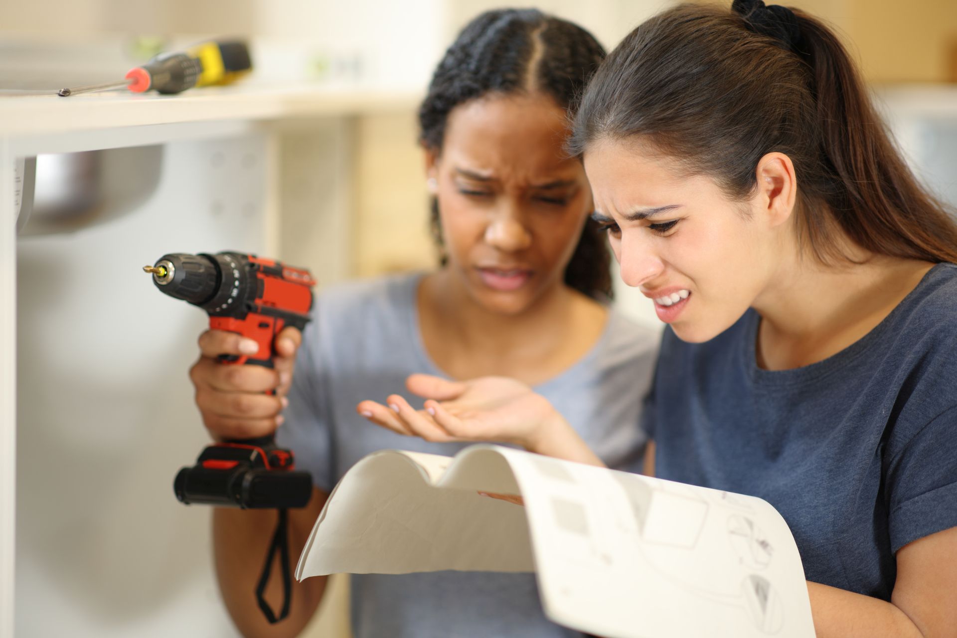Zwei Frauen beim Heimwerken, unsicher über die nächste Montageschritt, Betonschraube ohne Dübel als zuverlässige Lösung.