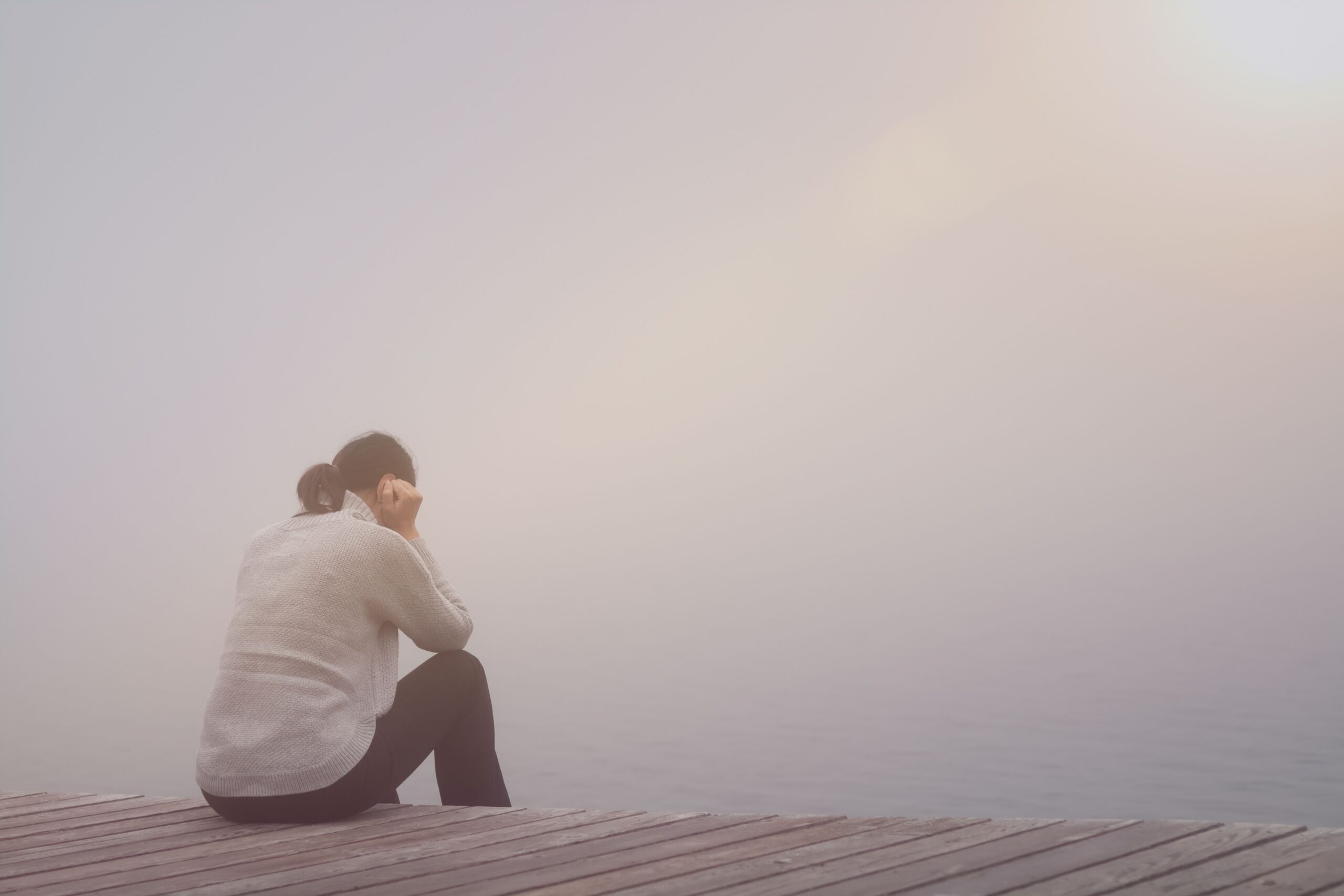 Nachdenkliche Frau allein am Steg – symbolisiert emotionale Belastung und Unklarheit