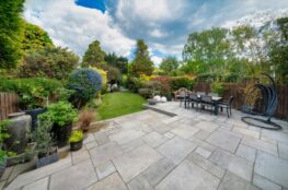 Gartenbau Mannheim Beispiel: Grosszuegige Terrasse mit Natursteinplatten, moderner Sitzgruppe und farbenfroher Gartengestaltung im Hintergrund