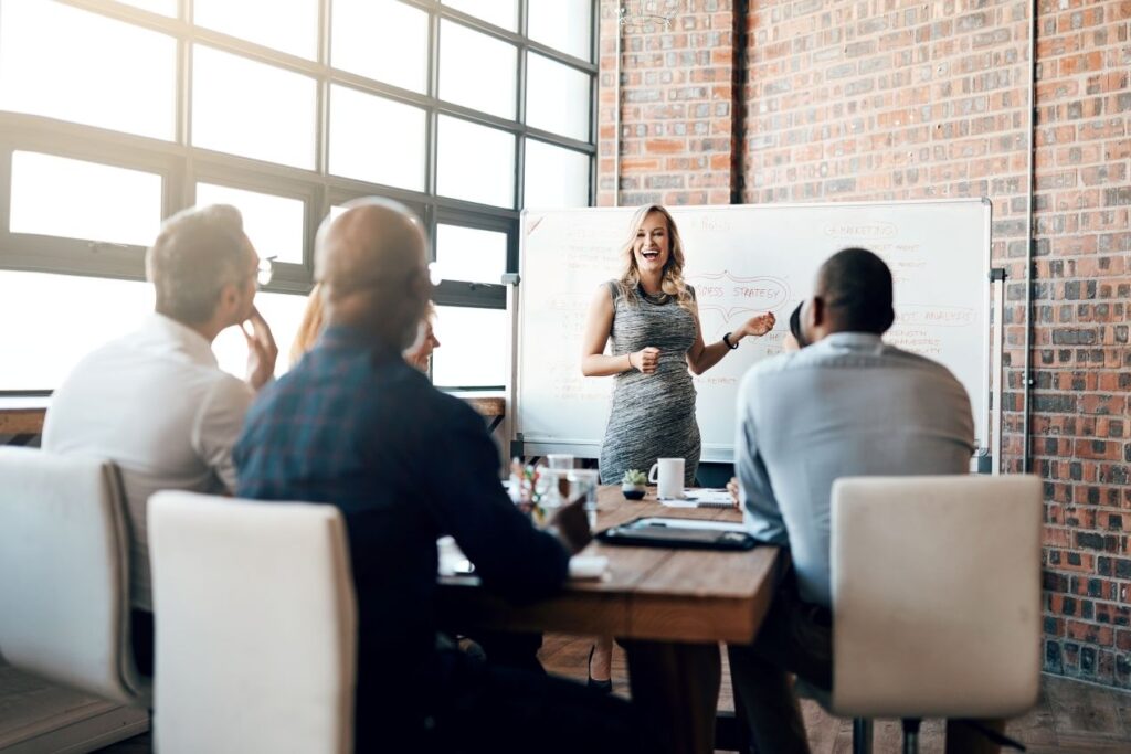 Frau moderiert ein Verhandlungstraining im Business-Kontext vor einem Team am Whiteboard mit Strategie-Notizen