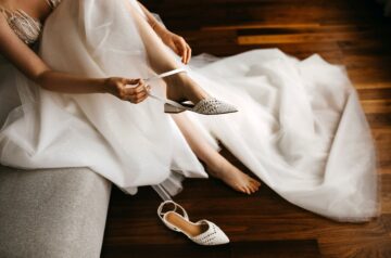 Brautschuhe mit Riemchen anziehen – elegante Braut in weißem Kleid bereitet sich auf die Hochzeit vor