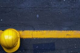 Gelber Schutzhelm liegt auf nasser gelber Linie einer Bodenmarkierung auf Asphalt – Symbol fuer Sicherheit und Struktur