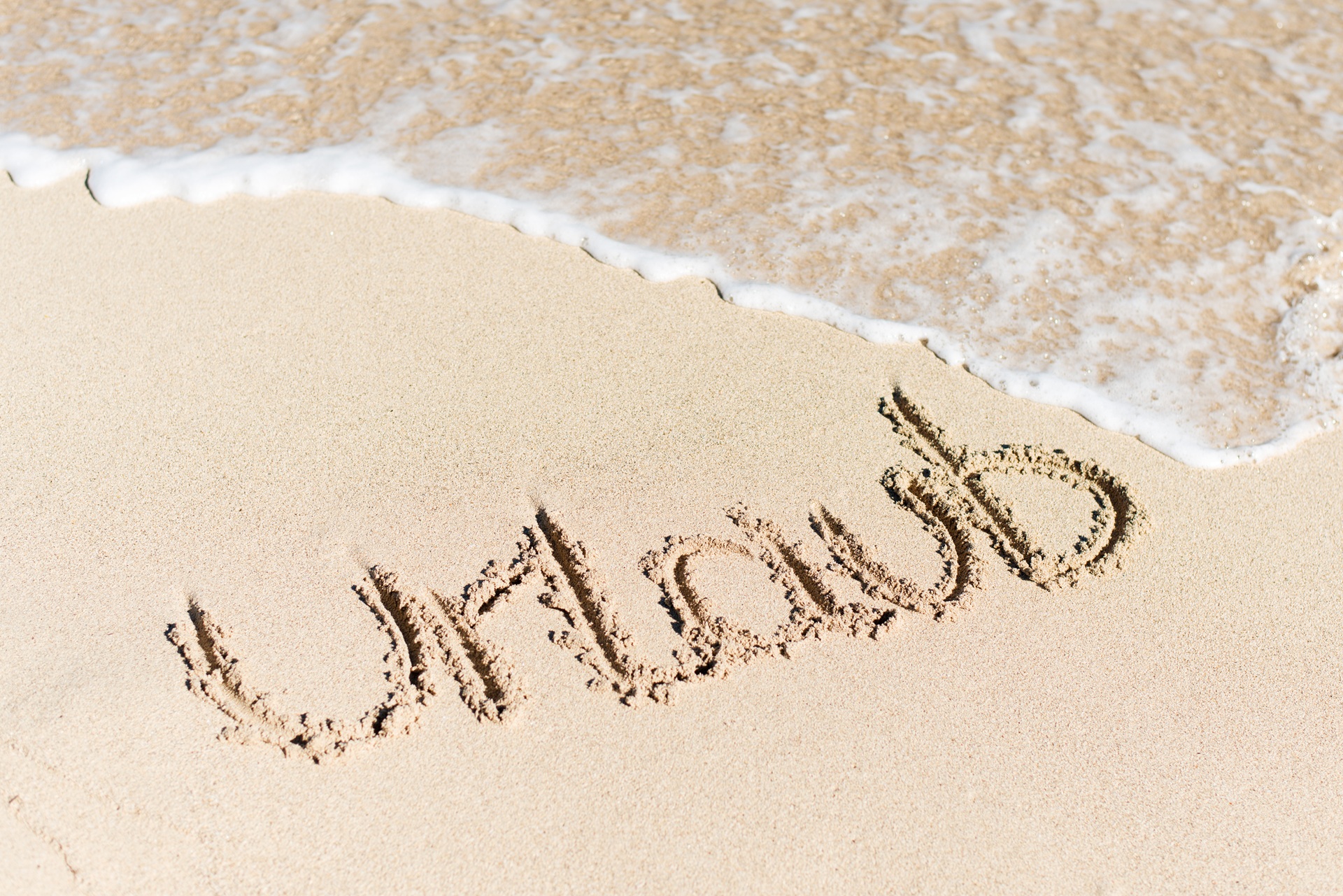 Wort Urlaub in den Sand geschrieben mit nahender Welle | Wellnesshotel Bayern