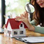 Frau prüft Modellhaus-Dach mit Lupe | Dachreinigung