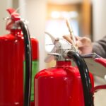 Techniker prüft zwei rote Feuerlöscher im Gebäude | Sachverständiger Löschanlagen
