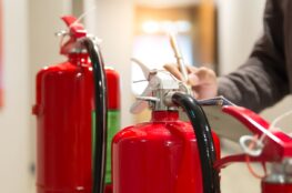 Techniker prüft zwei rote Feuerlöscher im Gebäude | Sachverständiger Löschanlagen